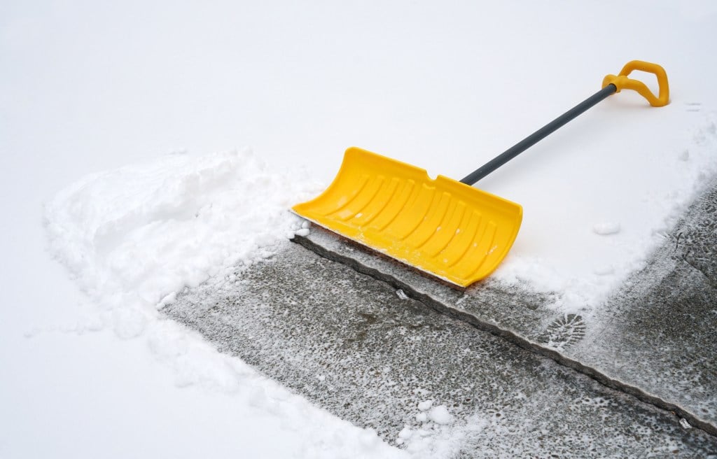 Snow on driveway with a yellow shovel.